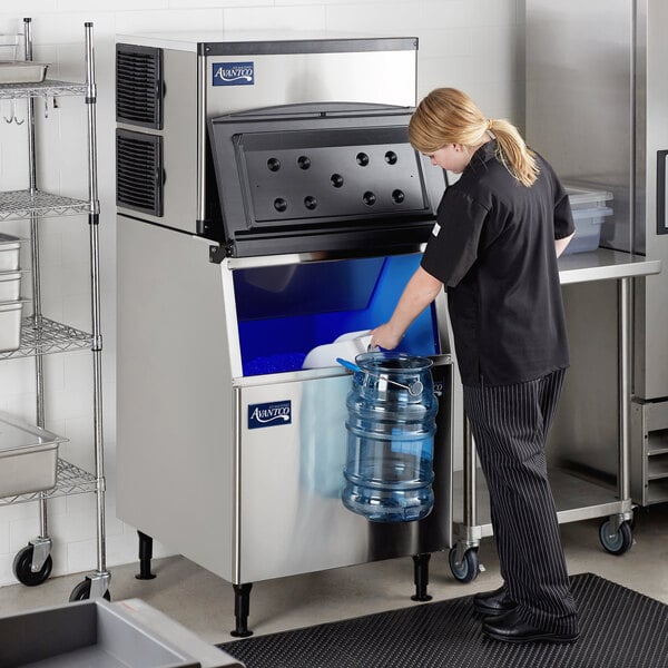 A woman in striped pants standing in a school kitchen using an Avantco air cooled ice machine to fill a water bottle.