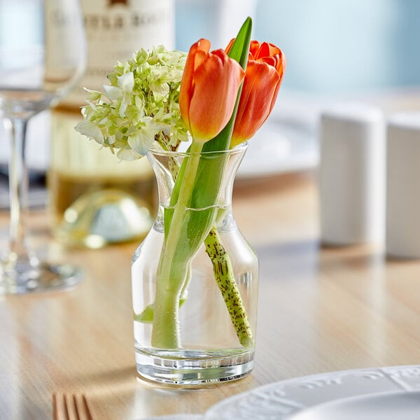 An Acopa urn glass bud vase with flowers on a table.