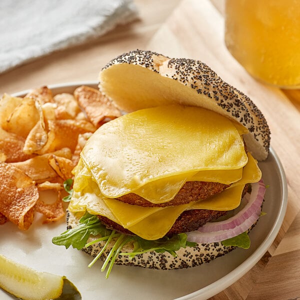 A cheeseburger with Follow Your Heart vegan provolone cheese, pickles, and potato chips on a plate.