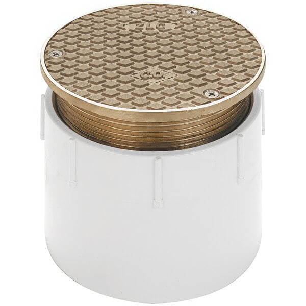 A white plastic pipe with a round metal lid with a square pattern and gold accents.