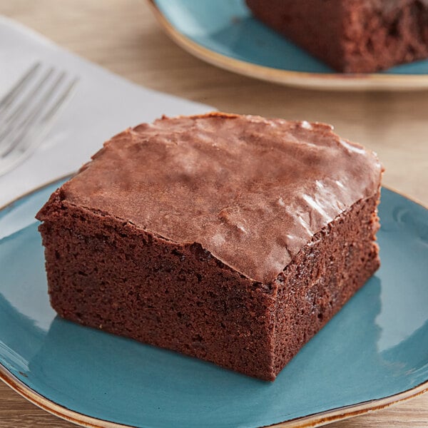 A brownie on a plate with a blurry hand in the background.