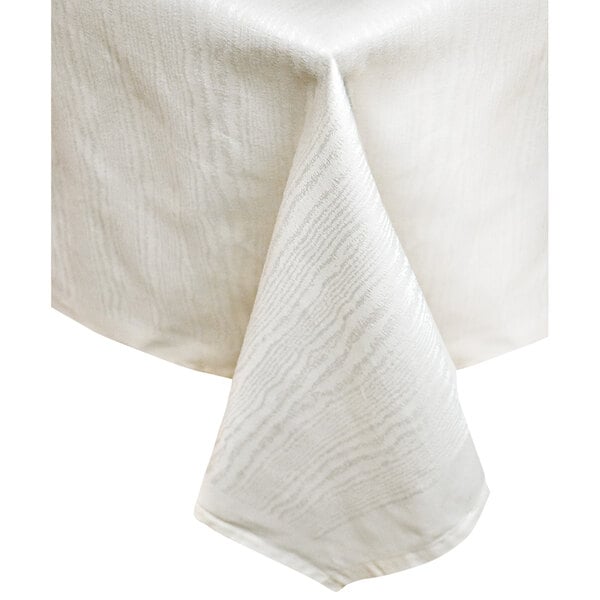 A folded white Garnier-Thiebaut Elm Crossbordered tablecloth on a table.
