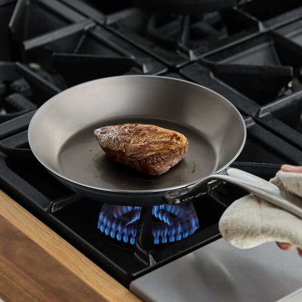 A person cooking a piece of meat on a de Buyer carbon steel fry pan.