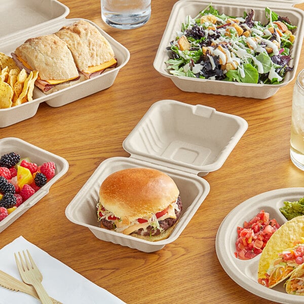 A table with EcoChoice natural bagasse plates and food containers with a sandwich, salad, and burger.