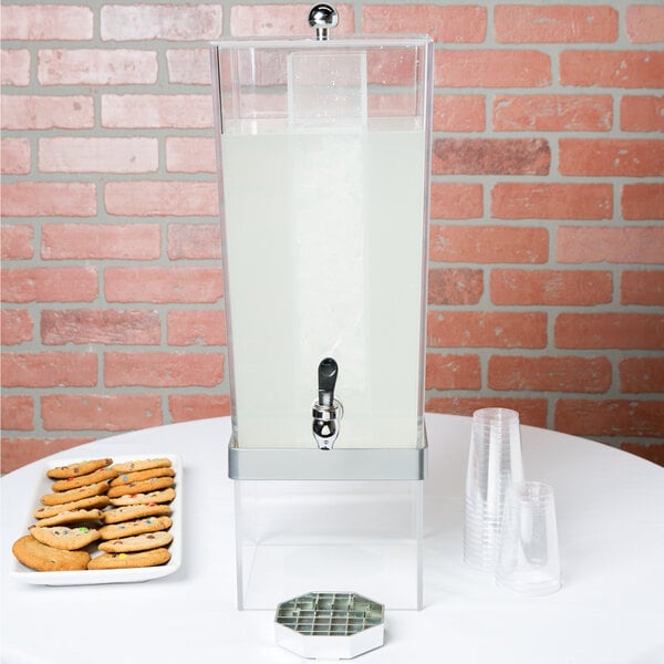 A silver Cal-Mil beverage dispenser with an ice chamber and cookies on a table.