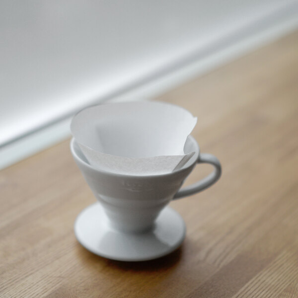 A white coffee cup with a Hario V60 paper filter inside.