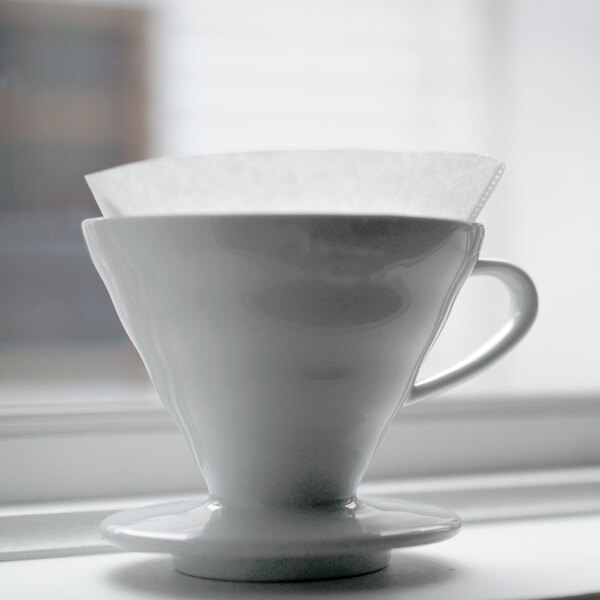 A white coffee cup with a Hario V60 paper filter over it.