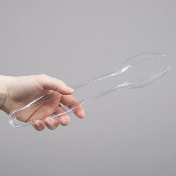 A hand holding a pair of clear plastic tongs.