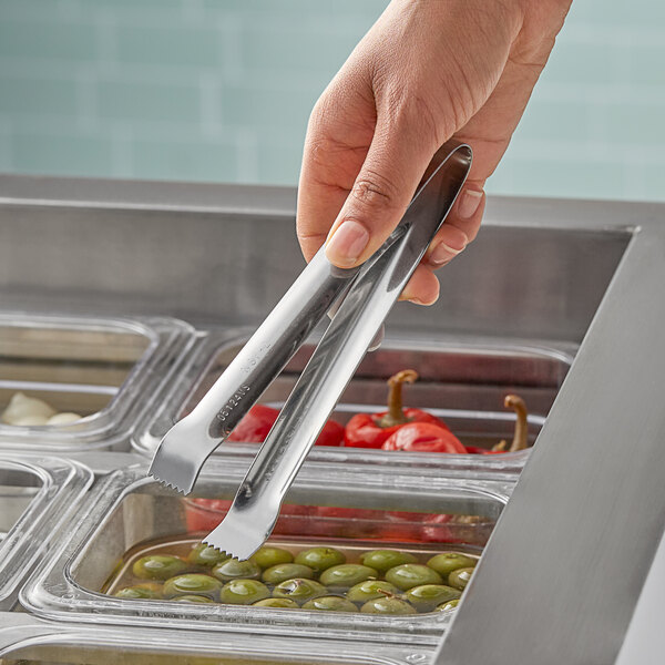 A person using Vollrath Pom Tongs to serve olives from a metal container.