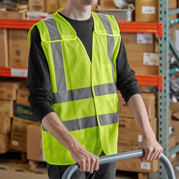 A person wearing a Lavex Class 2 lime yellow high visibility safety vest holding a hand truck.