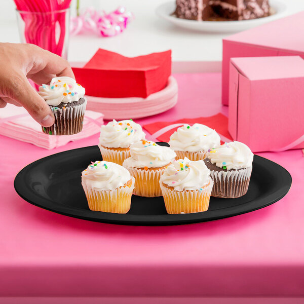 A person holding a cupcake on a black oval platter.