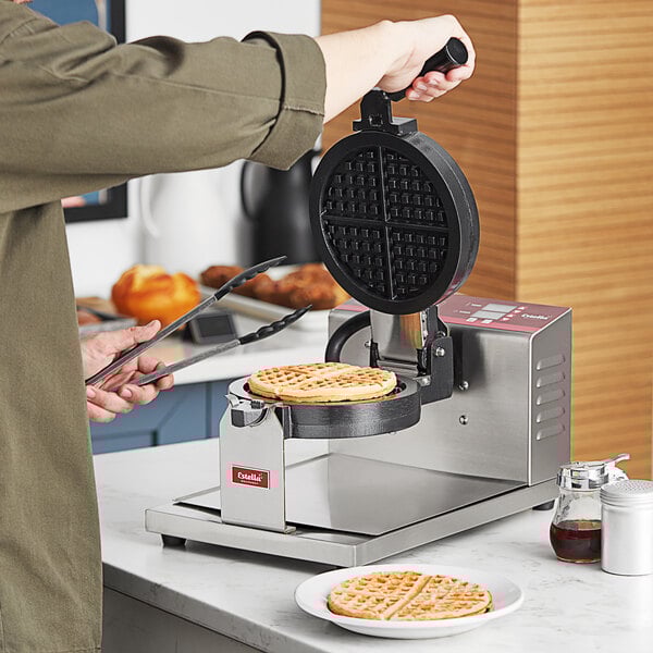 A person making waffles in a commercial Estella waffle maker.