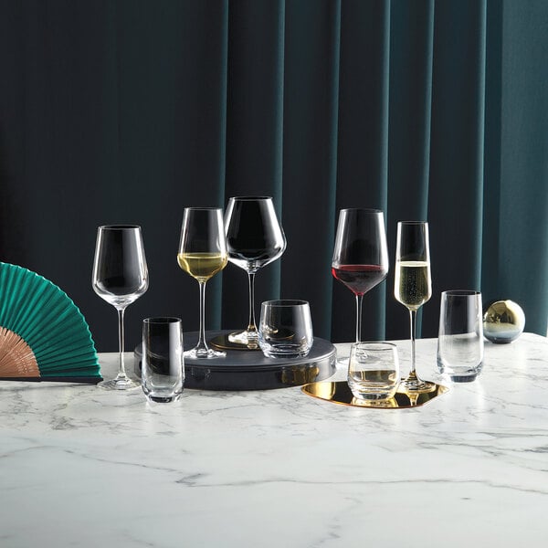 A set of clear 12.5 oz. rocks or double old fashioned glasses displayed on a marble surface with other assorted glassware.