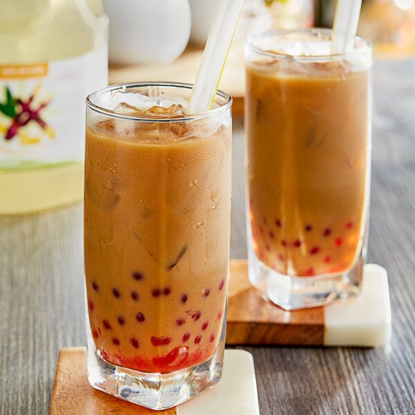 Two glasses of brown liquid with straws on a white surface.