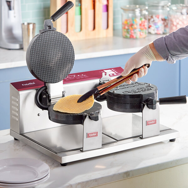 A person using a Estella double waffle cone maker on a counter.