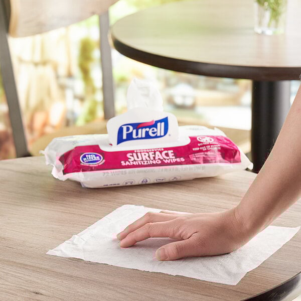 A hand using Purell Surface Wipes to clean a table at a hotel buffet.