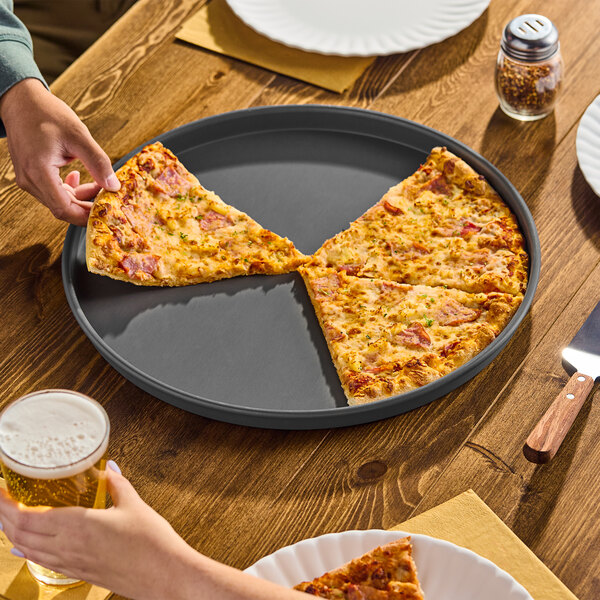 A round, straight-sided, hard coat anodized aluminum pizza pan with a partially eaten pizza on it.