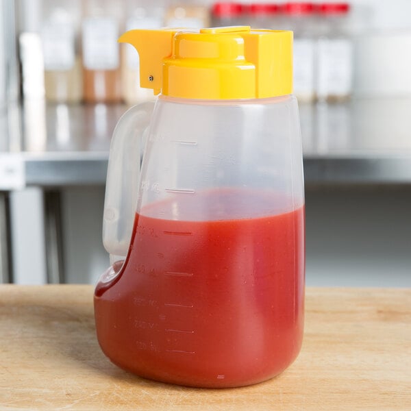 A Tablecraft plastic dispenser jar with a yellow lid on a table.