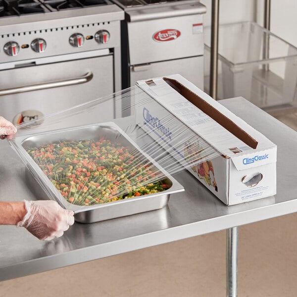 A person using Berry standard plastic wrap to cover a tray of vegetables.