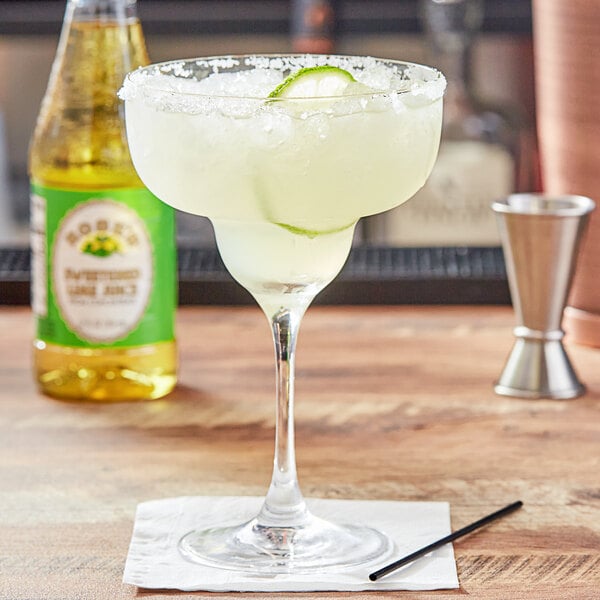 A margarita glass with a drink in it and a bottle of Rose's Sweetened Lime Juice on a table in a Mexican restaurant.