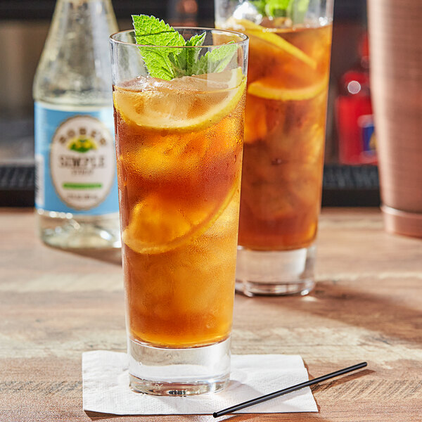 A bottle of Rose's Simple Syrup on a table with two glasses of iced tea with lemons and mint.