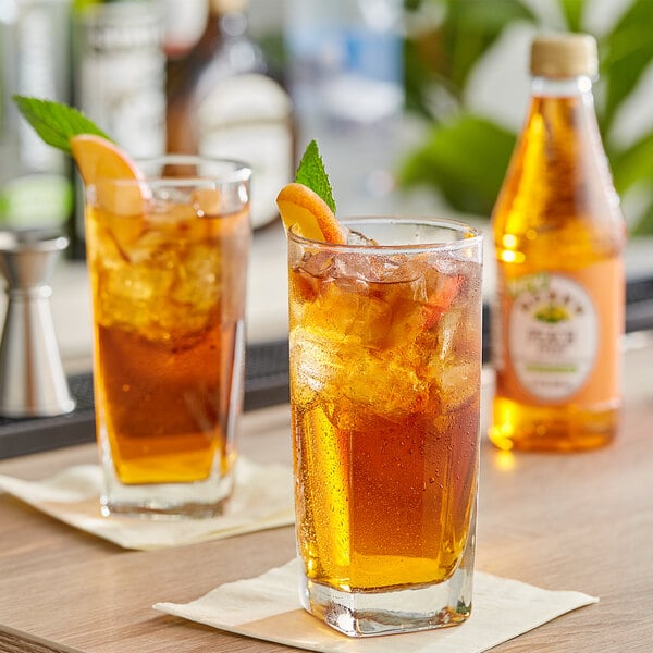 A glass of Rose's peach syrup mixed with ice and orange liquid.