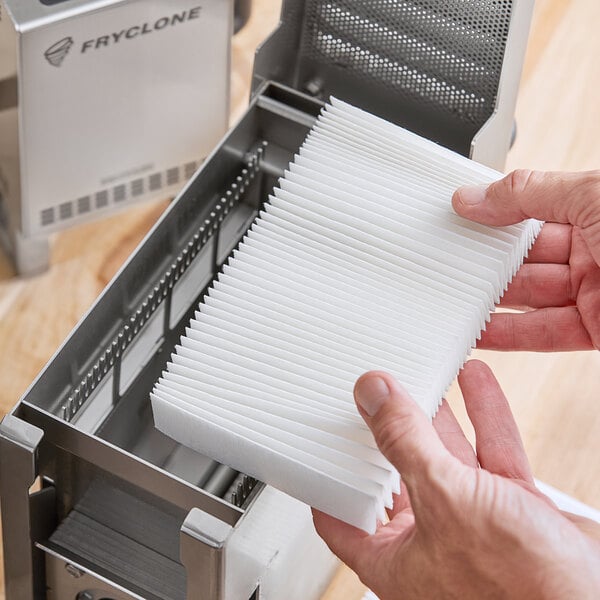 A person holding a stack of white Fryclone Fryer Oil Particle Filters.