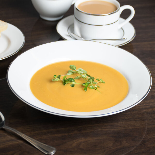 A white 10 Strawberry Street Silver Line porcelain soup bowl on a table with a bowl of soup.