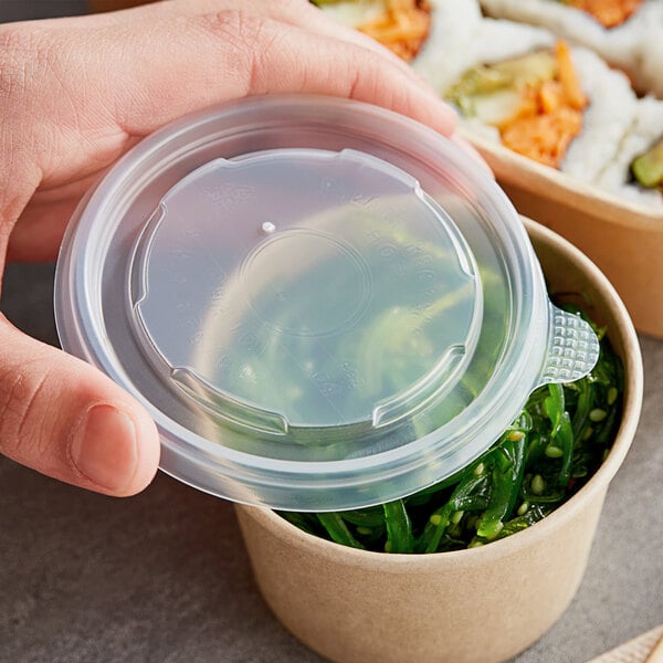 A hand holding a Choice plastic lid over a container of food.