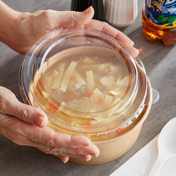 Hands holding a Choice PET take-out lid on a plastic container of soup.