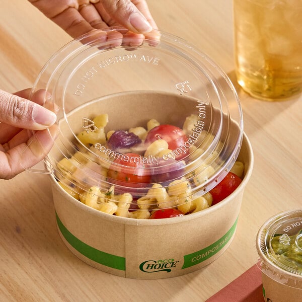 A clear round compostable PLA take-out lid being placed on a brown paper food container.