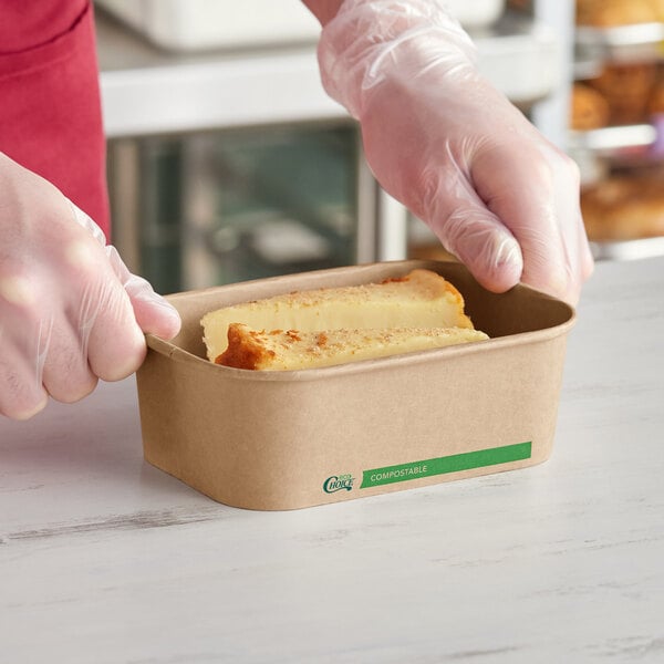 A rectangular kraft compostable take-out container holding a slice of cake.