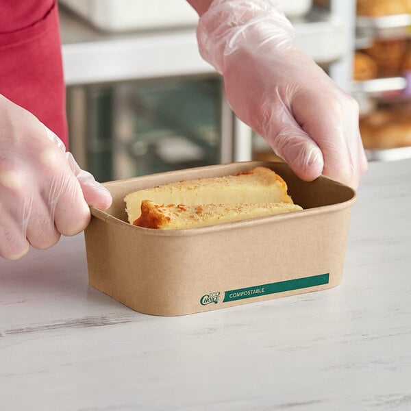 A person holding a piece of bread in an EcoChoice rectangular cardboard take-out container.