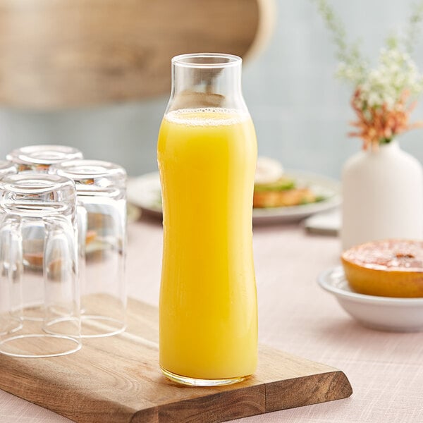 A Libbey glass swerve bottle filled with orange juice on a table.