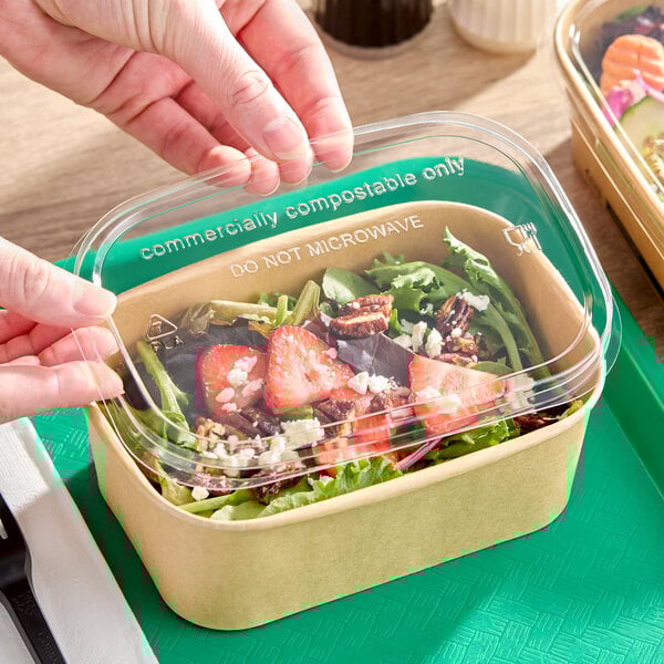A clear rectangular compostable PLA take-out lid being placed on a cardboard food container.