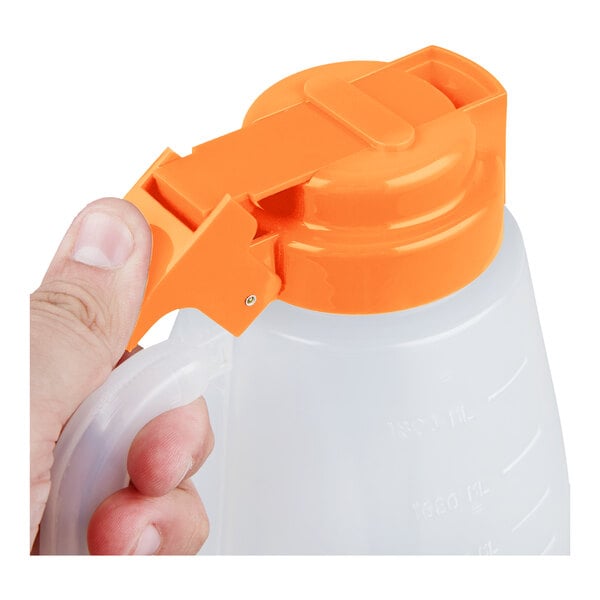 A translucent plastic dispenser jar with an orange lid and handle, being held by a hand.