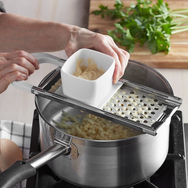 chef using spaetzle maker over a boiling pot of water