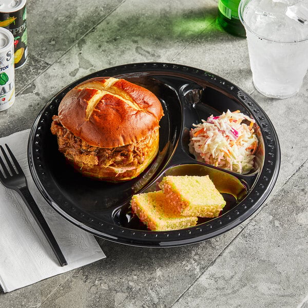 A sandwich and cornbread on a Huhtamaki Chinet black plastic 3 compartment plate.
