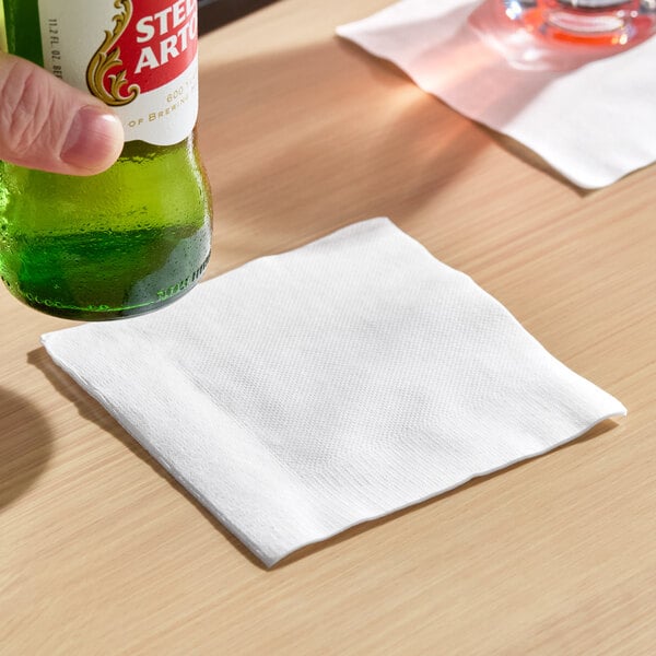 A plain white 1-ply beverage or cocktail napkin on a wooden surface.