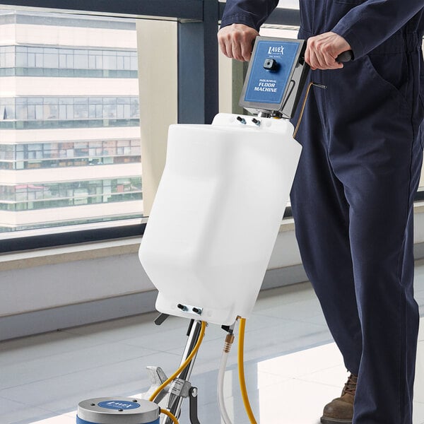 A person in blue overalls uses a Lavex solution tank on a floor cleaning machine.