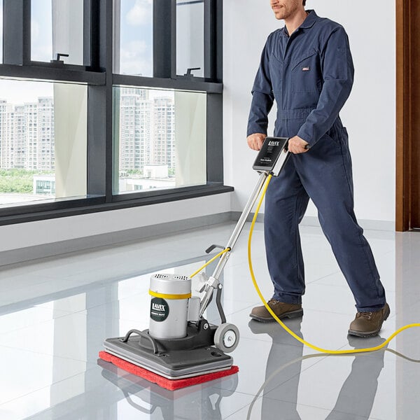 A man in blue coveralls using a Lavex Pro rectangular floor machine to clean a floor.