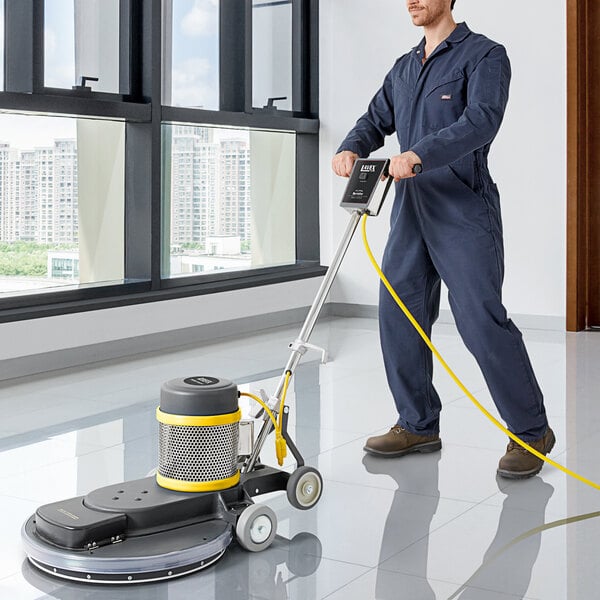 A man in a blue coverall using a Lavex Pro floor burnisher to polish a floor.