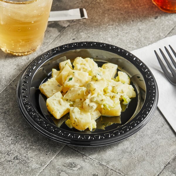 A Huhtamaki Chinet black plastic plate filled with food on a table.