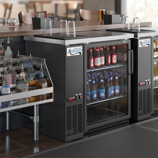 An Avantco back bar cooler on a counter filled with bottles of beer and liquor.