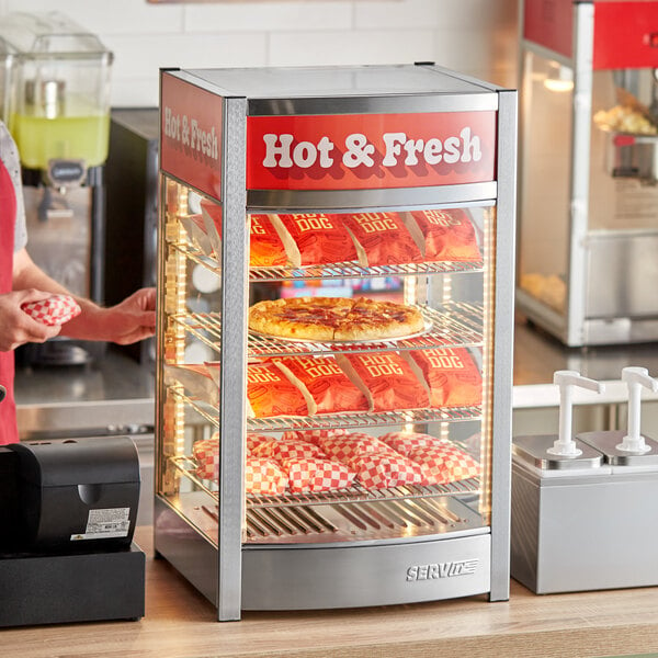 A woman standing in front of a ServIt countertop hot food display with pizza on the shelves.