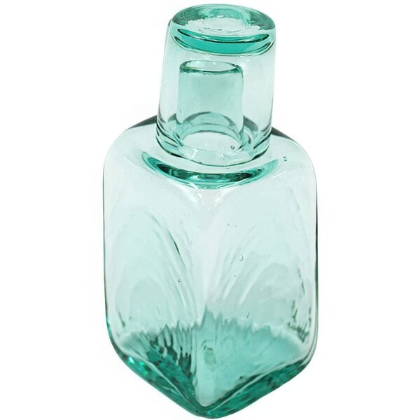 A close-up of a clear square glass carafe with a top and a small square glass.