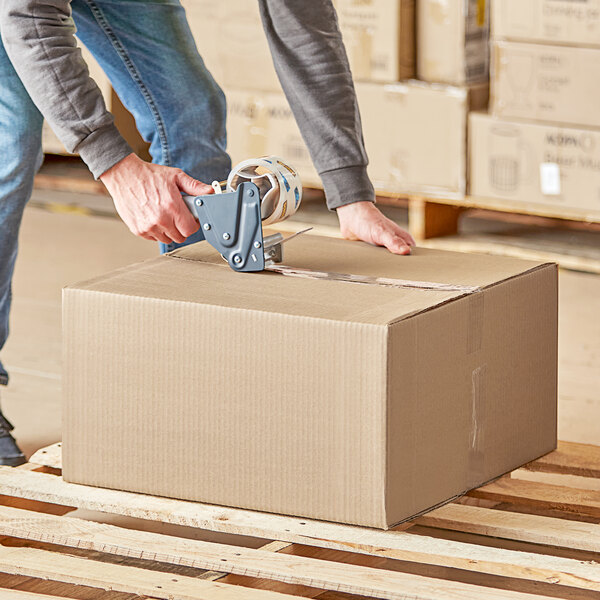 A person using a box cutter to cut a Kraft corrugated shipping box.