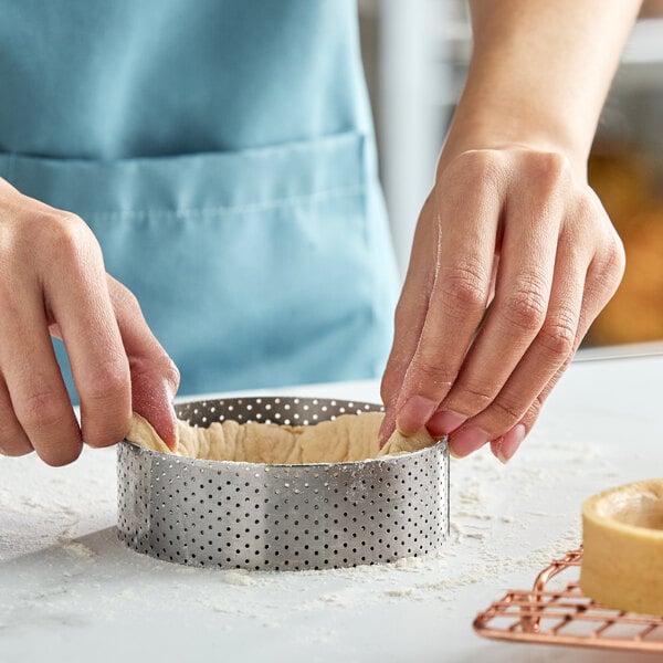 A perforated stainless steel tart ring being used to shape dough.