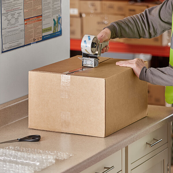 A person in a safety vest packing a Lavex Kraft shipping box.