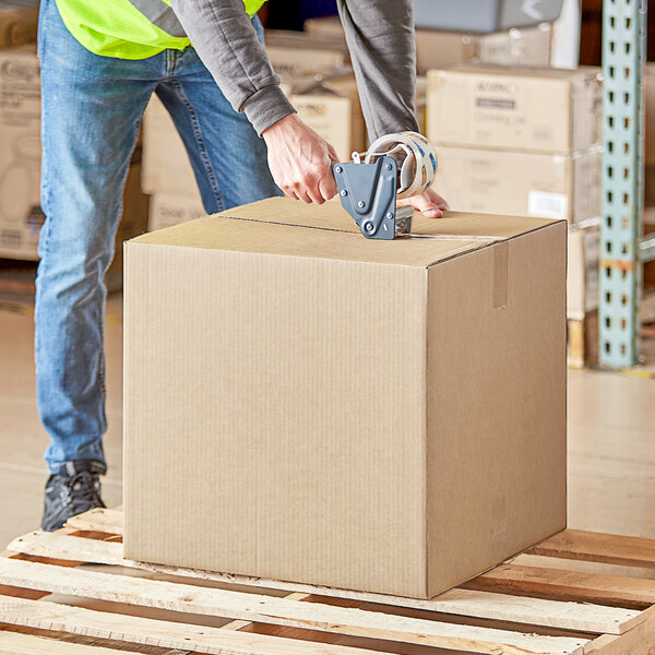 A person wearing a safety vest using a box cutter to cut a box.